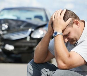 man sitting keeping his palms on head near to his damaged car