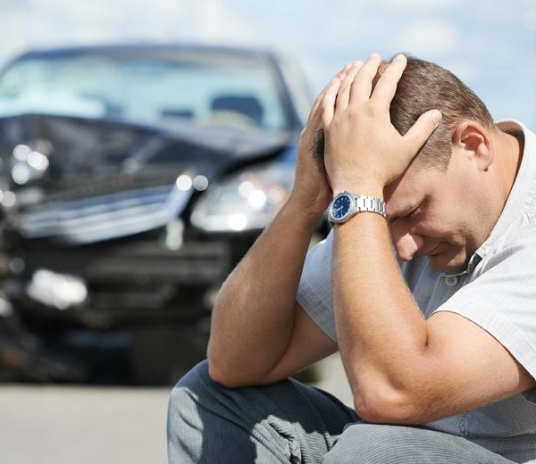man sitting keeping his palms on head near to his damaged car