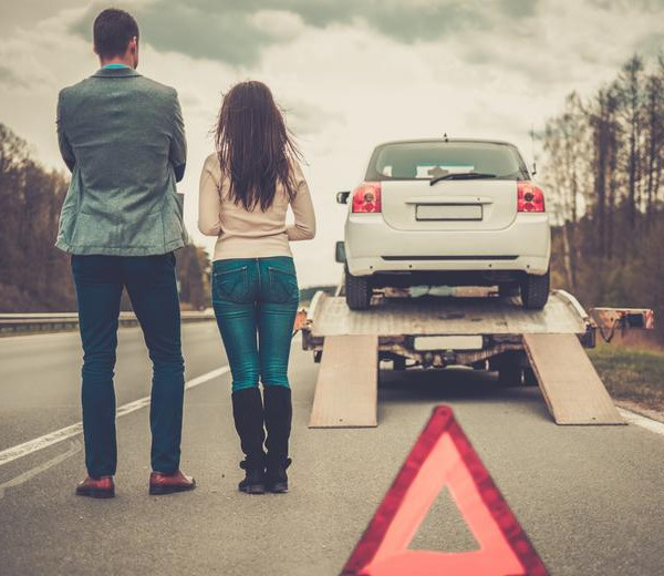 a man and women standing backward looking at the car toeing with a crane